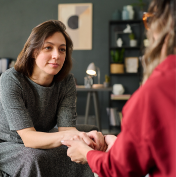 A supportive moment between two women holding hands, symbolizing connection, empathy, and emotional support. The image represents compassion, resilience, and the importance of mental well-being.